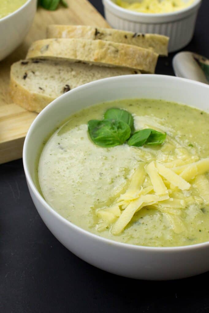 Broccoli and cauliflower soup in a bowl topped with cheddar, some pieces of bread on the table and on the cutting board | Hurry The Food Up