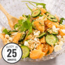 Cantaloupe and cucumber salad sits in a large glass bowl with wooden serving spoon on a grey, marbled table with a time stamp is in the bottom left hand corner | Hurry The Food Up