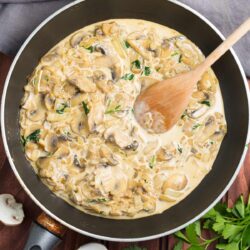 Cooked mushrooms in a big pan. Next to it, there are grey tablecloth, a bunch of parsley, and two pieces of mushrooms | Hurry The Food Up