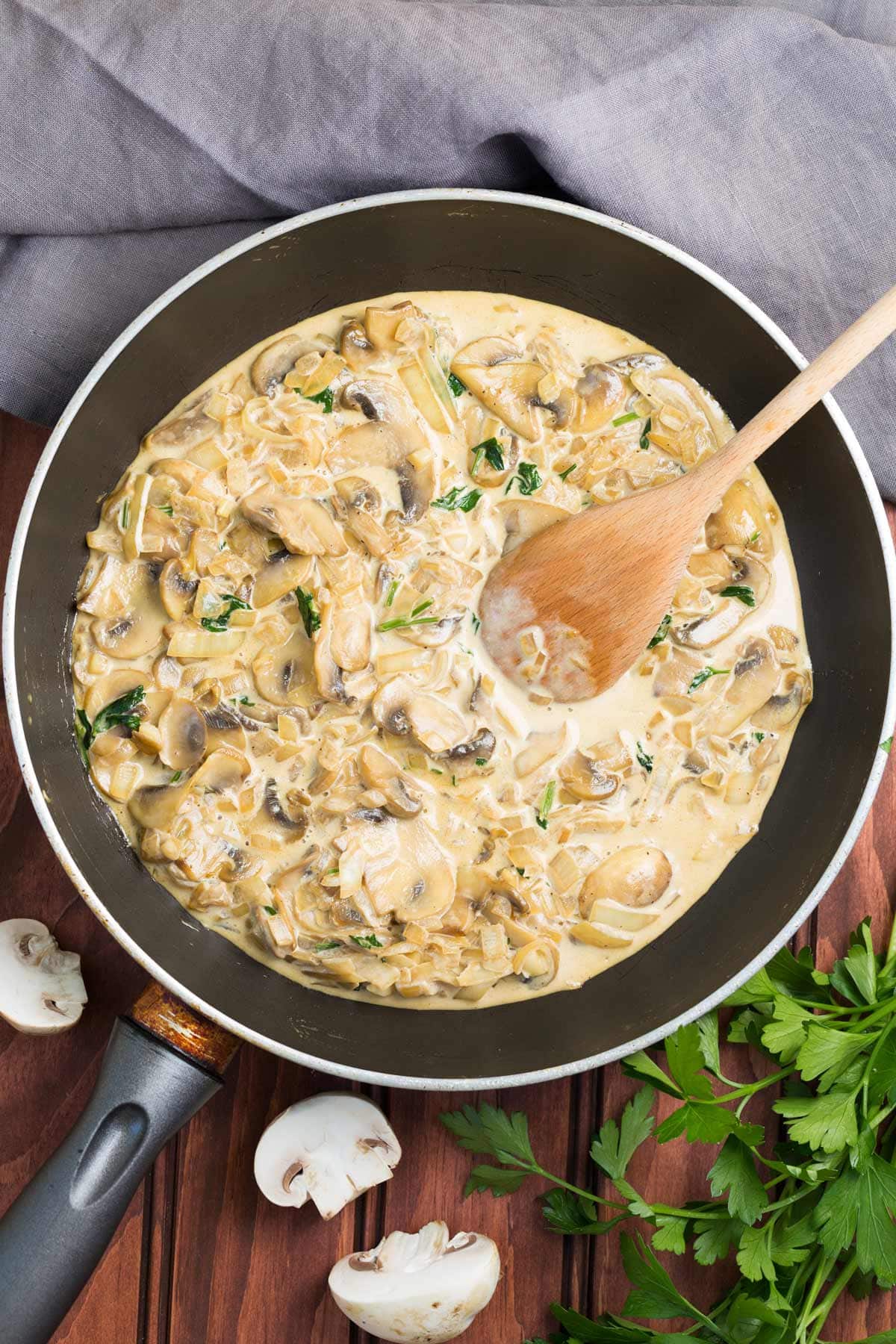 Cooked mushrooms are in a big pan. Next to it, there are grey tablecloth, a bunch of parsley and three pieces of mushrooms | Hurry The Food Up