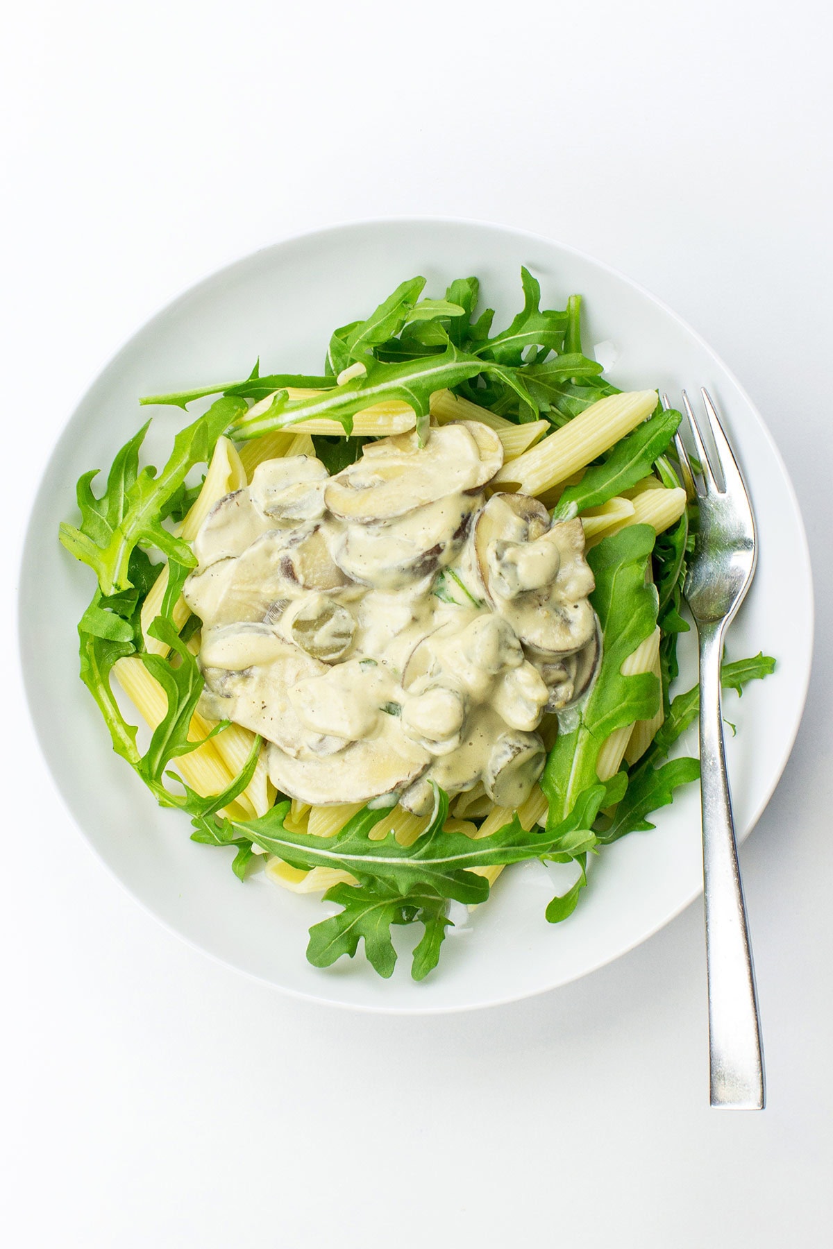 A bowl of creamy vegan mushroom pasta topped with fresh arugula.