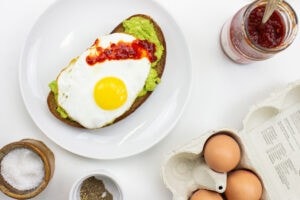 The avocado toast is on the plate on a table with salt, pepper, eggs and Sriracha in the jar #lemon #olive oil | 