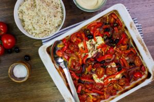 The dish is on the baking tray on a towel on a table with hummus, tomatoes, olives and a plate with rice | Hurry The Food Up