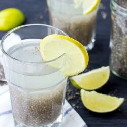 A glass of chia fresca (iskiate) placed on a white towel is seen with a slice of lime on its rim. Two other glasses and lime slices are in the distance | Hurry The Food Up