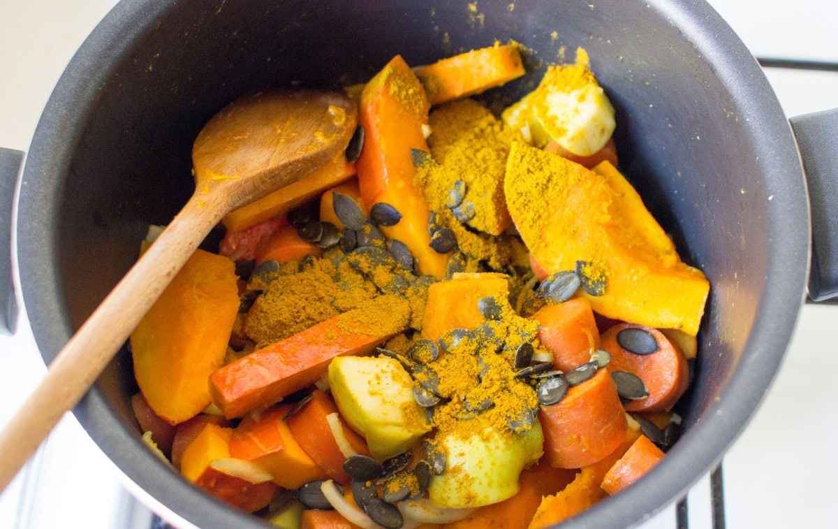 Large dark pot with cut pumpkin, carrots, apple, curry powder, and pumpkin seeds | Hurry The Food Up