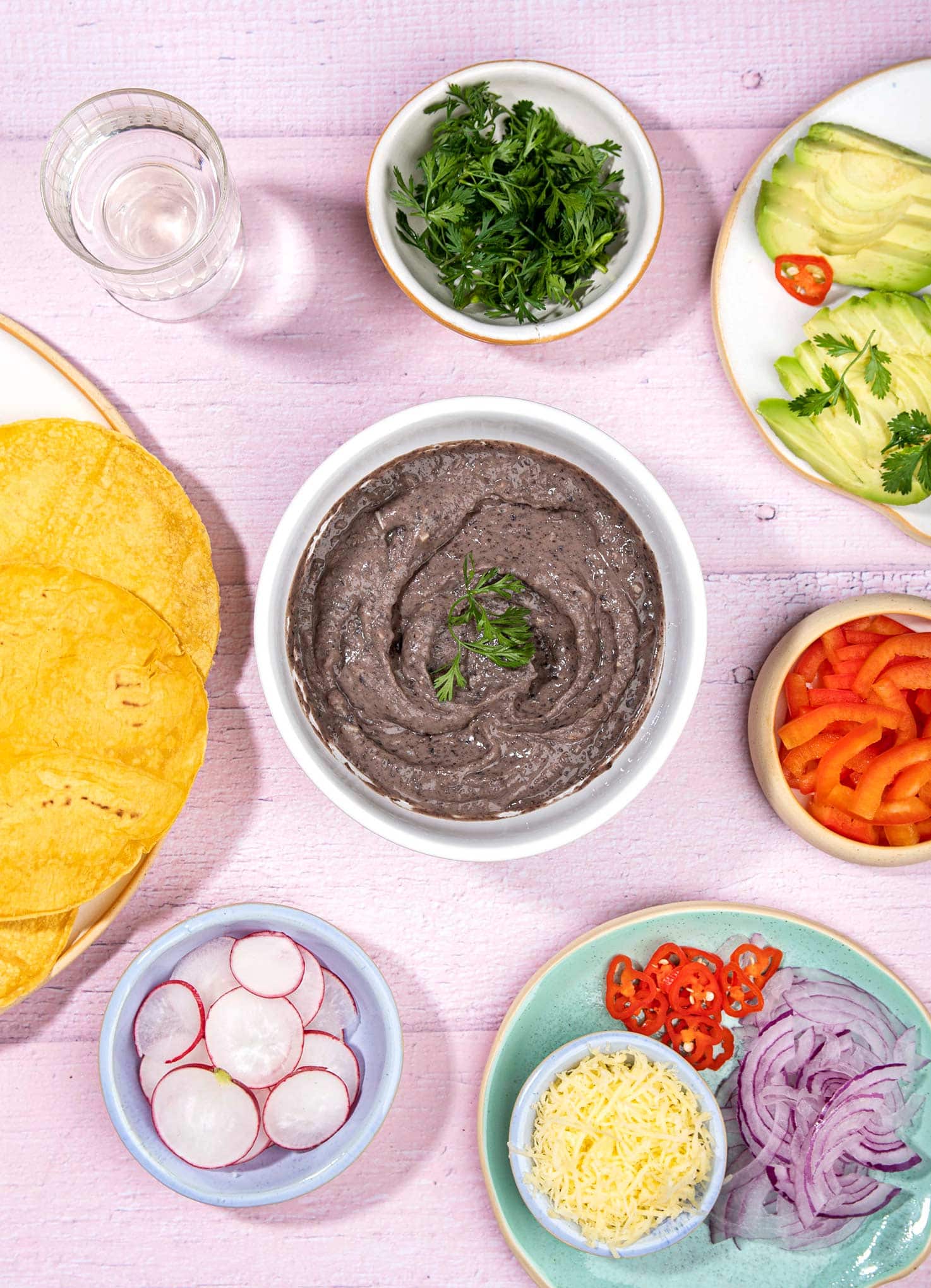 Bean dish is in the white bowl that is on the table with tortillas, cilantro, sliced radishes and avocado | Hurry The Food Up