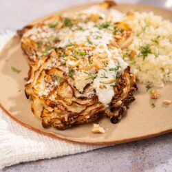 cabbage steaks topped with panko breadcrumbs on a ceramic plate. Sitting on a cream cloth on top of a stone table | Hurry The Food Up