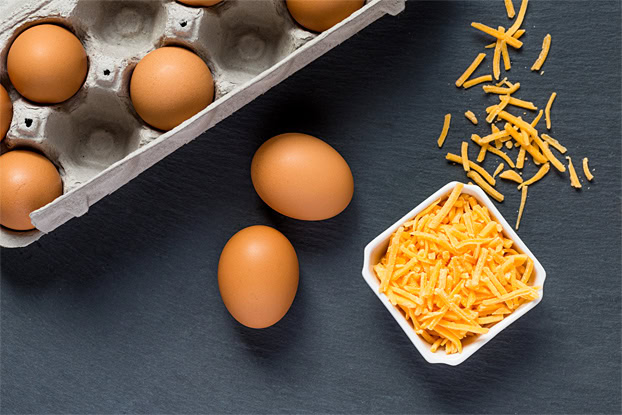 A few eggs with grated cheddar are on a black surface | Hurry The Food Up