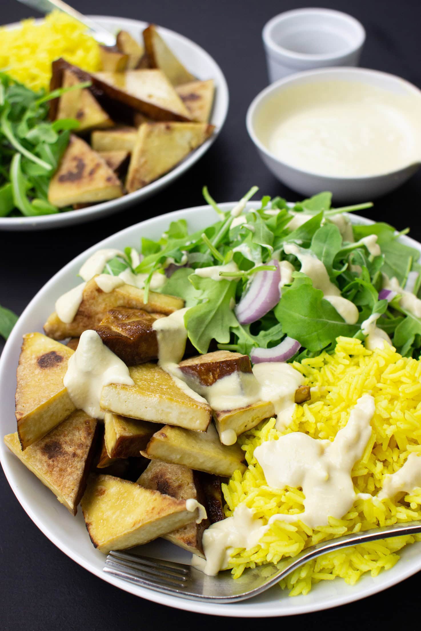 Smoked Tofu & Hummus Buddha Bowl with lamb’s lettuce are on the black table on 2 plates with forks, pepper and hummus #smoked tofu #olive oil | 