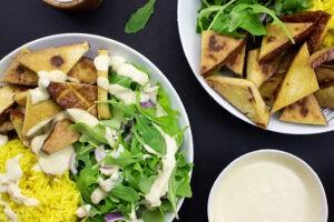 The Buddha Bowl with lamb’s lettuce are on the black table on 2 plates with forks, pepper, salt and hummus #lamb’s lettuce #red onion | 