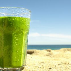 The glass of spinach banana smoothie is on beach | Hurry The Food Up