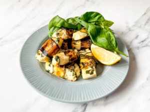 The dish is served with lemon and fresh basil on a plate on a white table #halloumi #zucchini | 