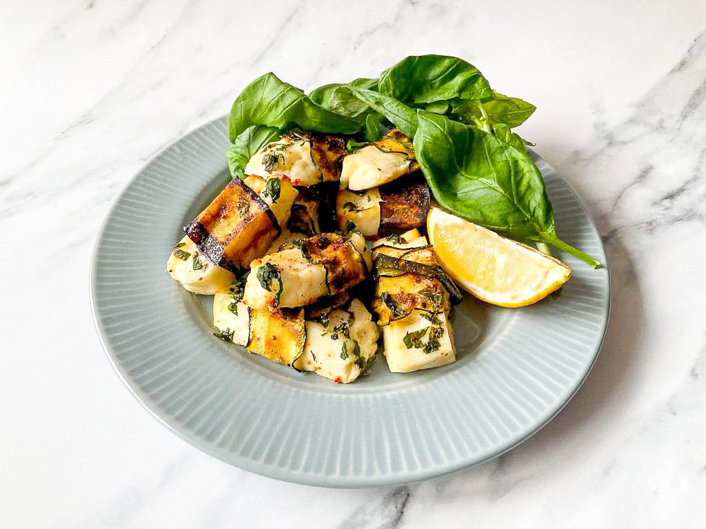 The dish is served with lemon and fresh basil on a plate on a white table #halloumi #zucchini | 