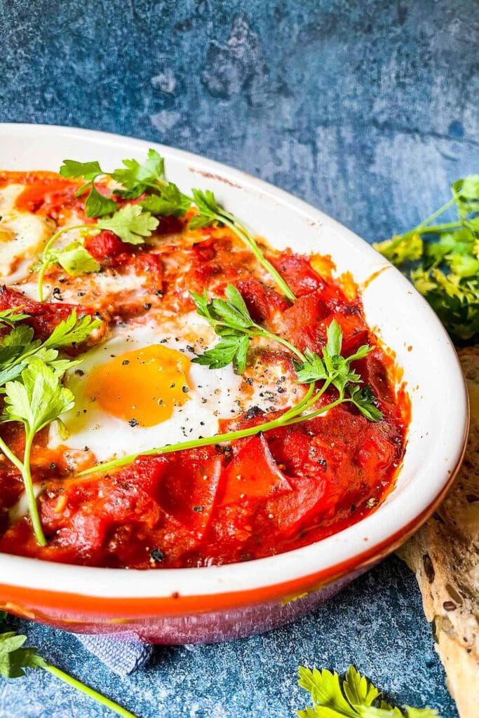 Vegetarian Shakshuka is served on the blue table with parsley and bread #eggs #red onion | 