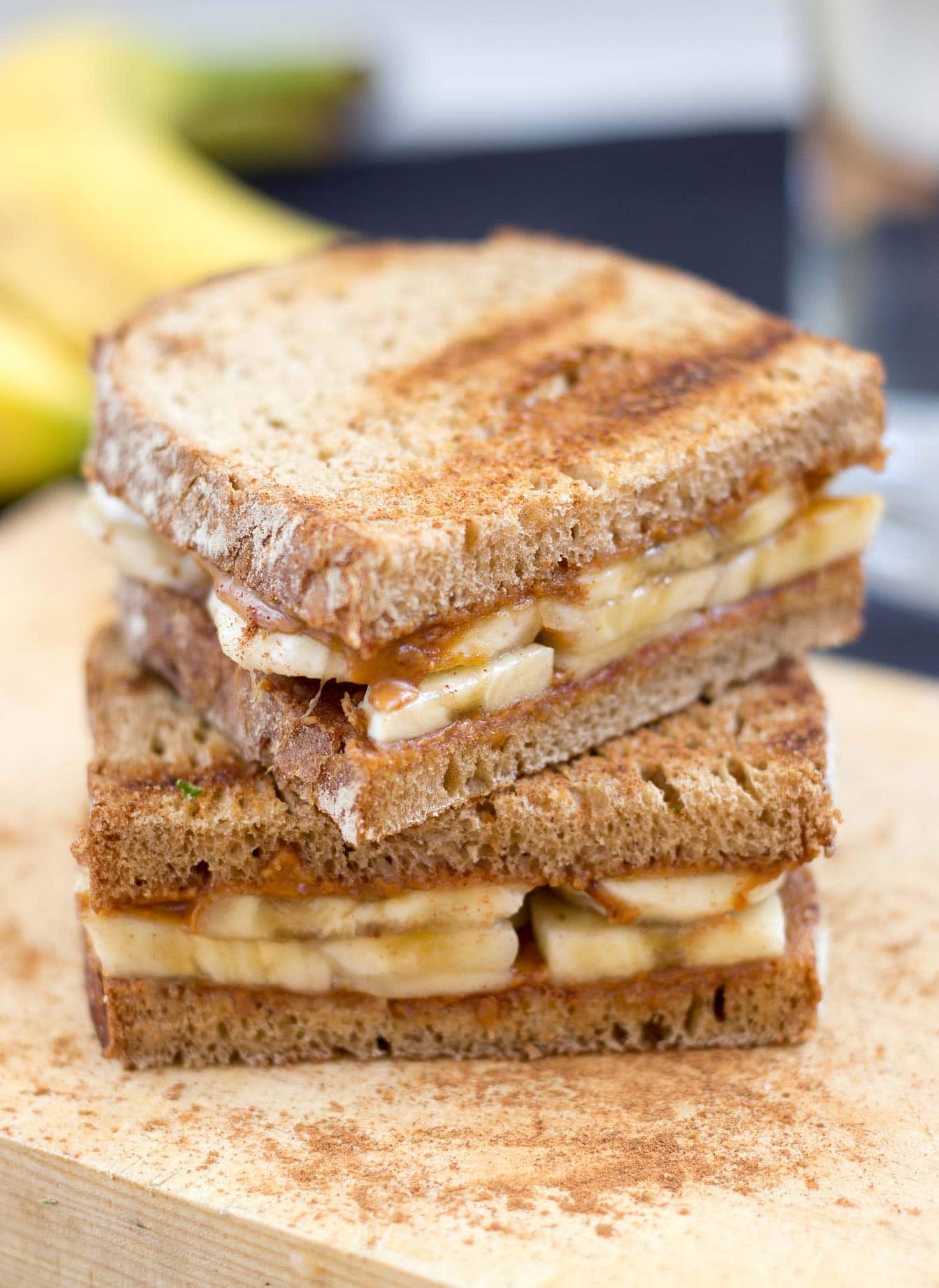 Two peanut butter and banana sandwiches are laid on the chopping board on the blue table with bananas | Hurry The Food Up