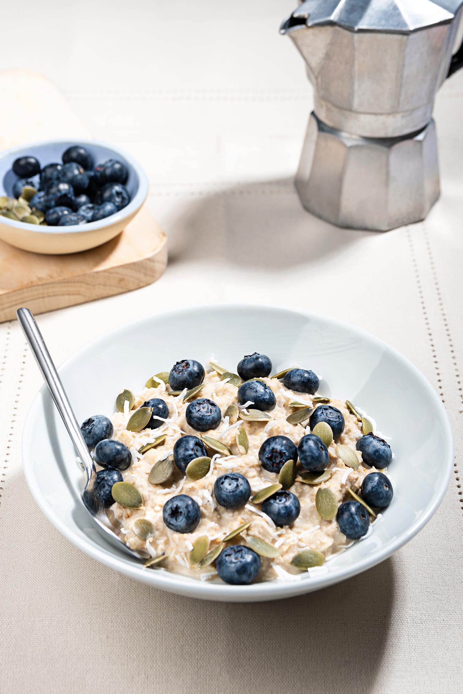 The Swiss muesli is in a bowl served with blueberries and pumpkin seeds, a coffee pot is in the right-hand corner | Hurry The Food Up