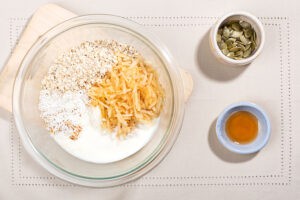 The oats, grated apple, coconut flakes and yougurt are in the bowl not mixed up, the pumpkin seeds and maple syrup are in separate small bowls on the right | Hurry The Food Up