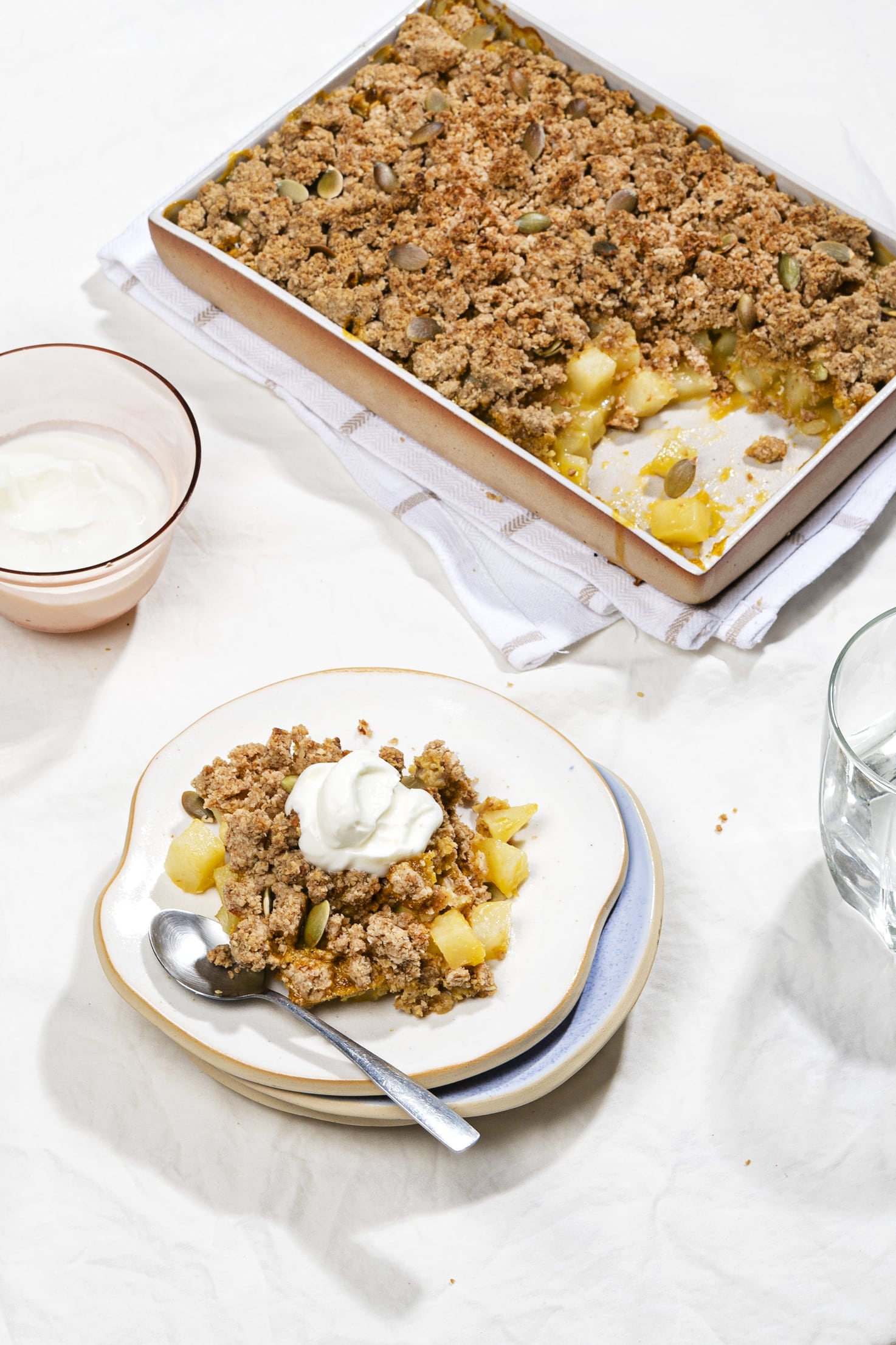 A serving of healthy pear crisp alongside the tray of crisp and a bowl of yoghurt. | Hurry The Food Up