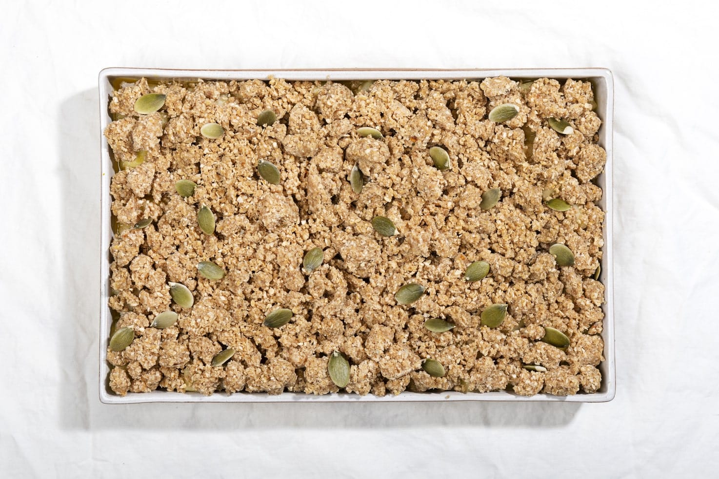 A tray of healthy breakfast pear crisp is laid out on a white surface, before it goes into the oven. | Hurry The Food Up