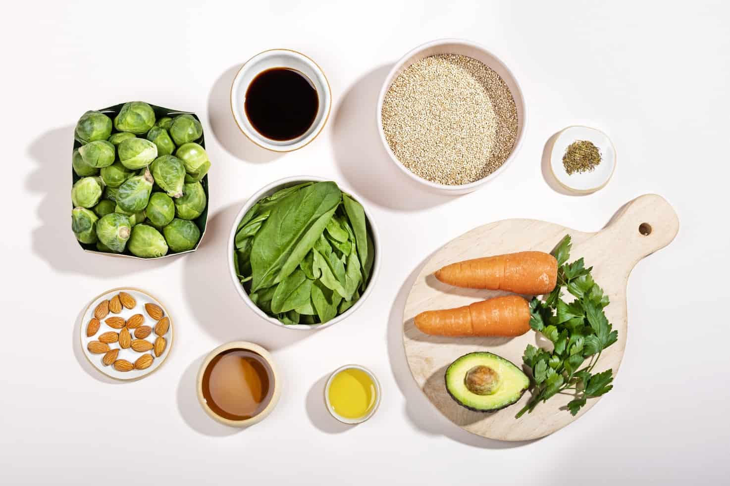 The ingredients for a Brussel sprouts and quinoa salad are laid out on a white surface. These include sprouts, spinach & quinoa.