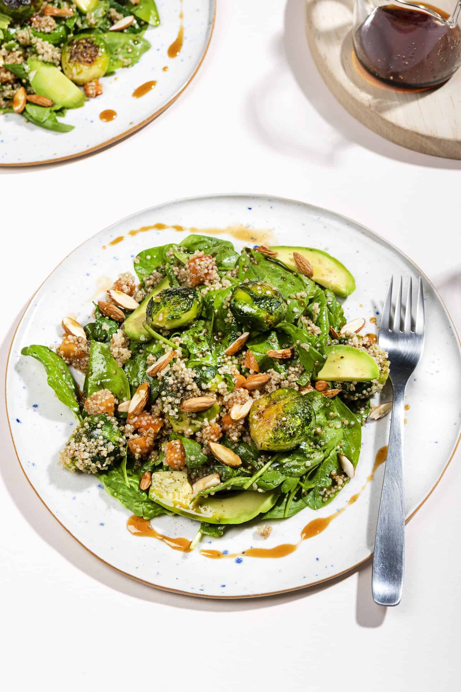 A plate of smashed brussel sprouts and quinoa salad, drizzled with dressing. A jug of dressing is nearby.