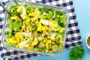 A glass bowl with cheese salad is on a checkered tablecloth. Near it, there are a bunch of parsley and a small white bowl | Hurry The Food Up