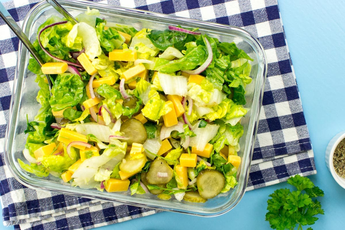 A transparent dish with cheese salad is on a checkered tablecloth. Near it, there are a bunch of parsley and a small white bowl | Hurry The Food Up