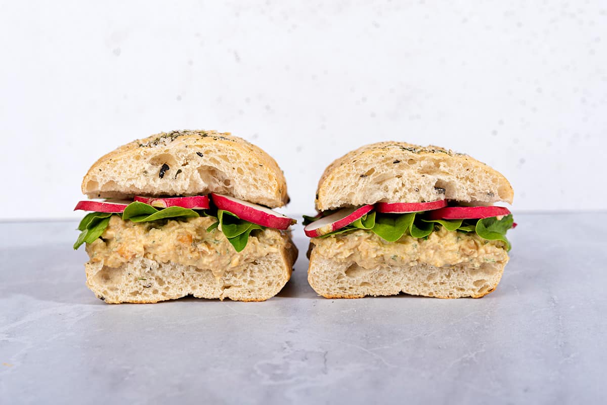 Two chickpea salad sandwiches are on a marble surface next to each other | Hurry The Food Up