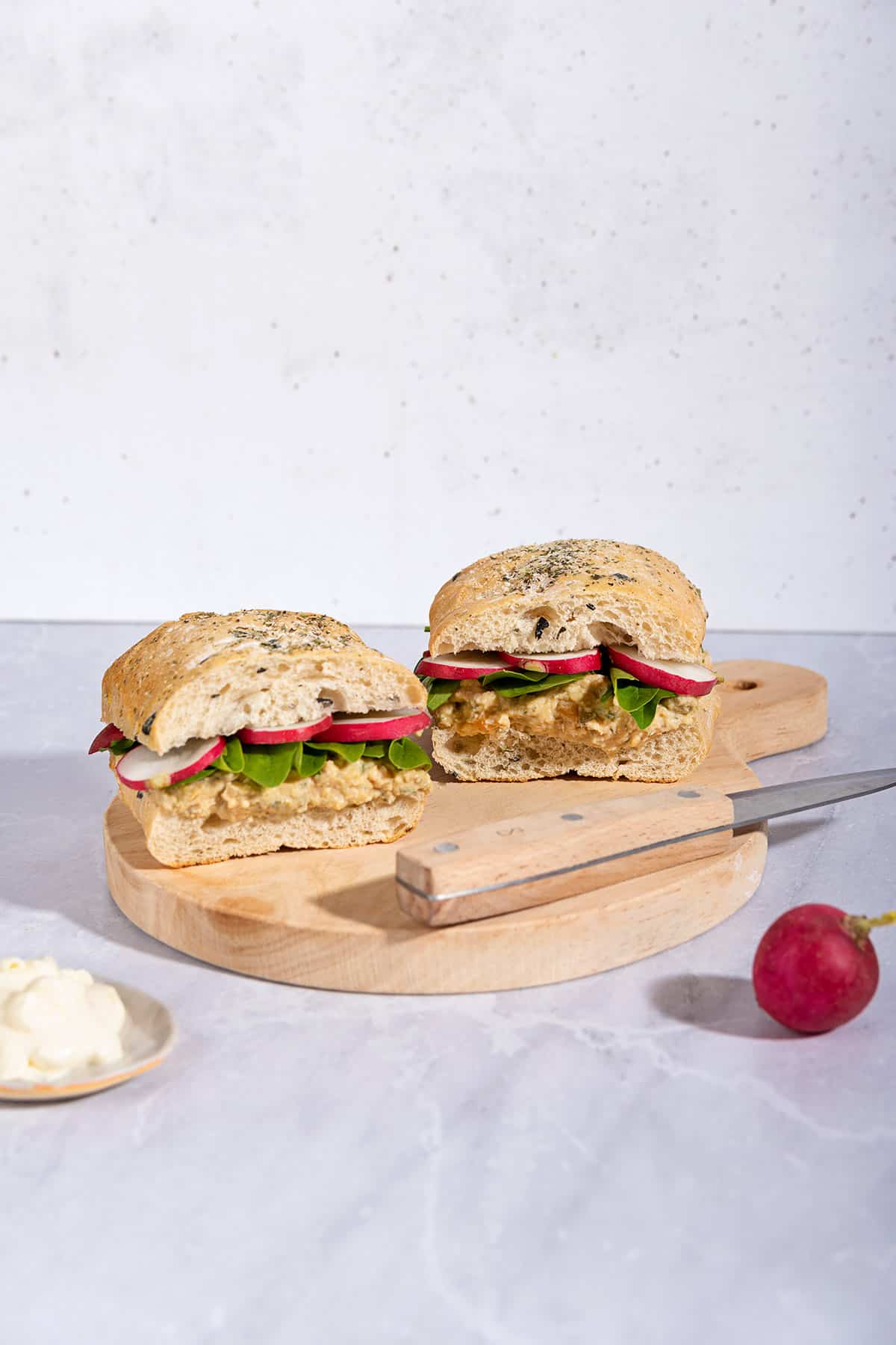 Two chickpea salad sandwiches with knife are on a wooden board that is on a marble surface | Hurry The Food Up