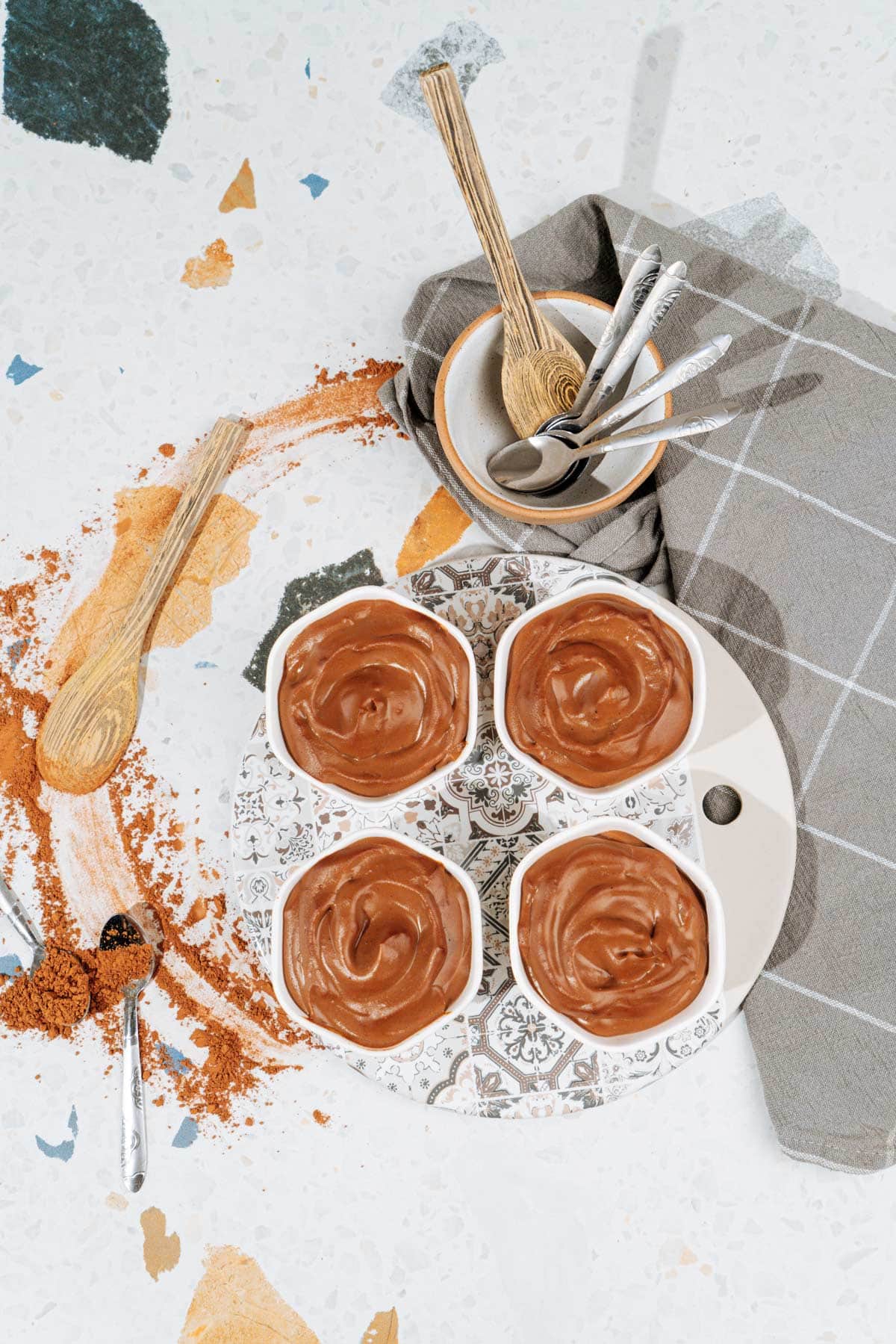 Bird's-eye view of chocolate protein pudding that is in the small white bowls. Near them, there is some cutlery | Hurry The Food Up
