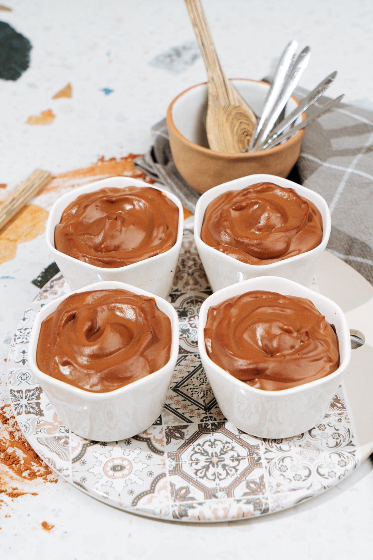 Four small white bowls with chocolate protein pudding stand on the plate. Behind them, there is a small wooden bowl with other cutlery | Hurry The Food Up