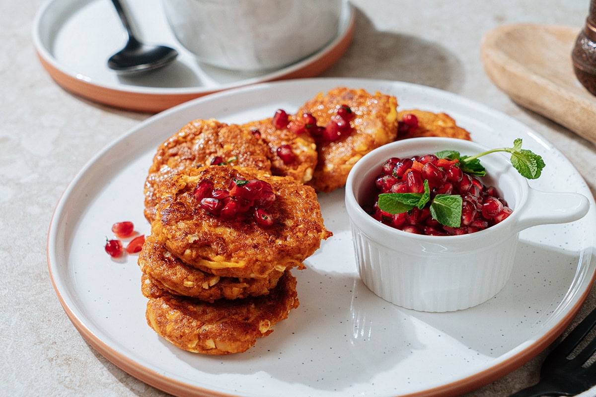 Roasted cottage cheese fritters are served on the white plate with a small dipping bowl of pomegranate salsa near them | Hurry The Food Up