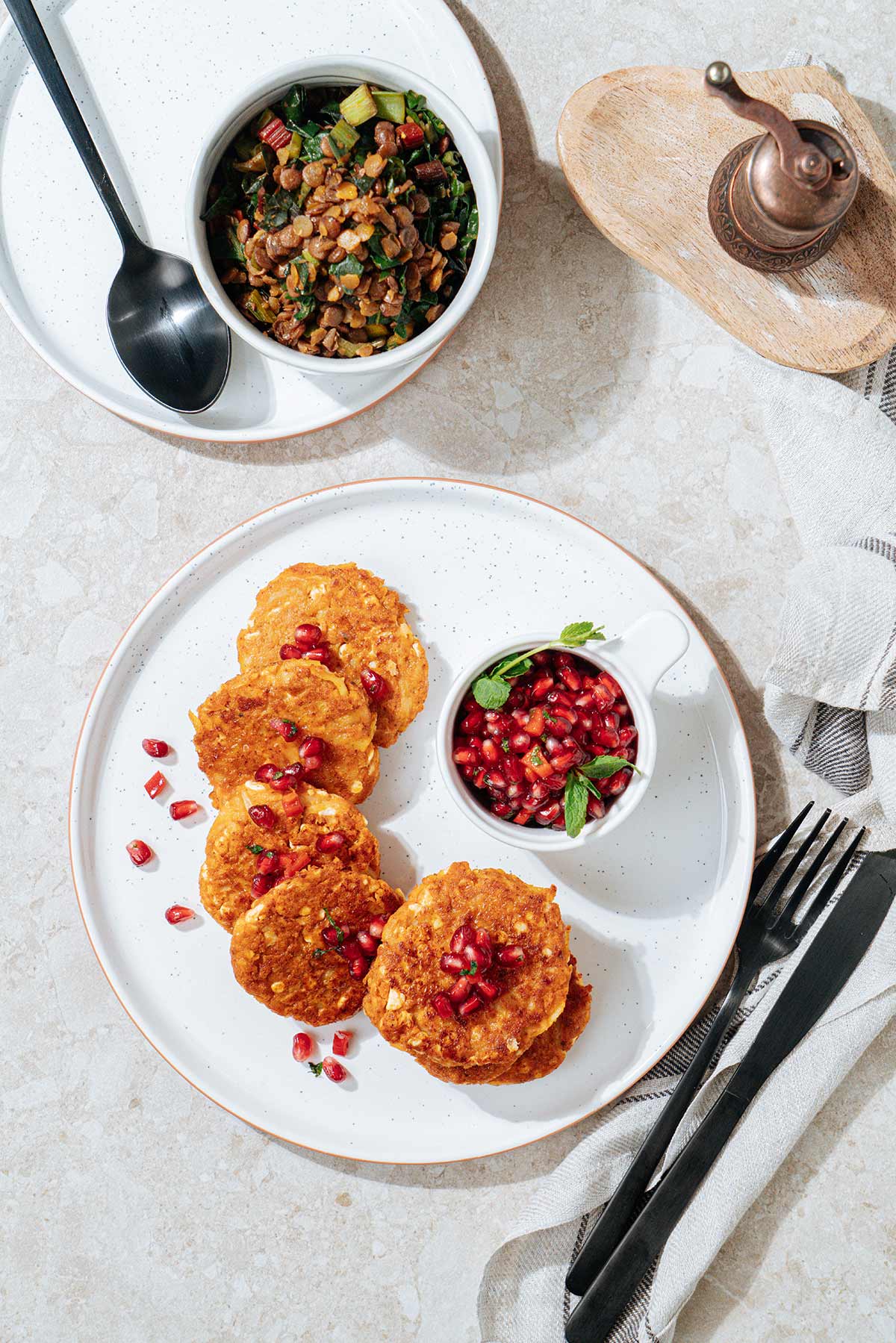 Bird's-eye view of roasted cottage cheese fritters that are served on the white plate with a small dipping bowl of pomegranate salsa near them. Next to it there is a lentil chard side is in the small white bowl | Hurry The Food Up