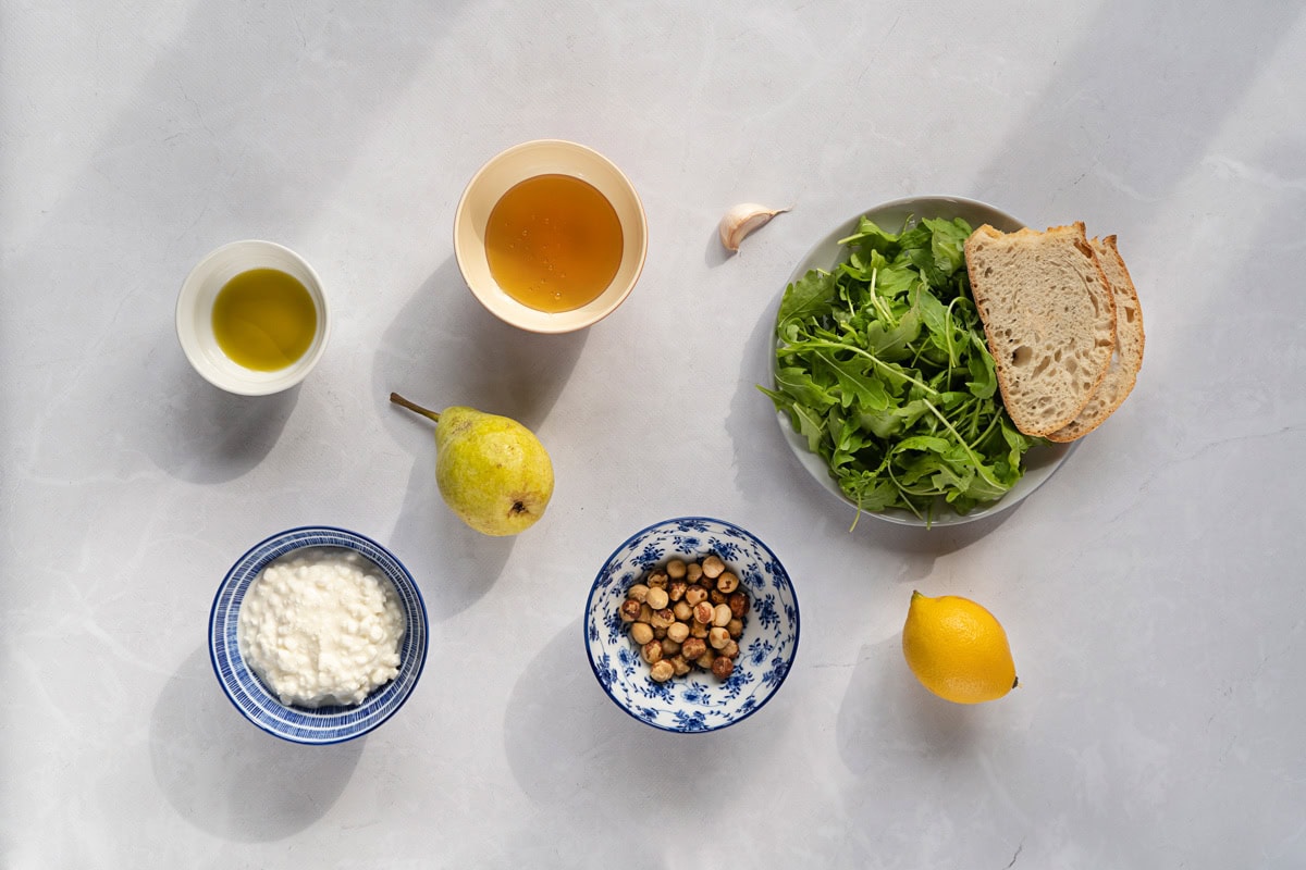 Cottage cheese salad ingredients like cottage cheese, hazelnut, garlic, lemon, olive oil, honey, arugula, bread, pear | Hurry The Food Up