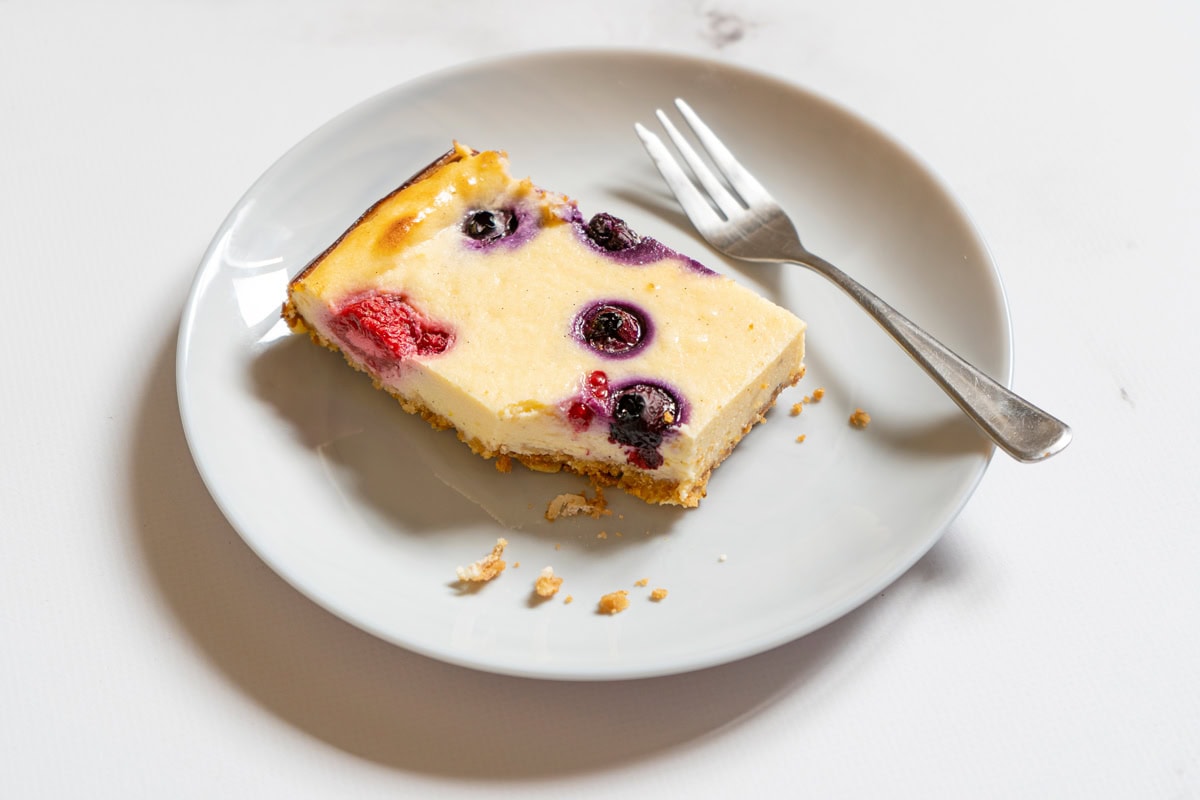 A white plate with a piece of cottage cheesecake and a fork on the marble surface | Hurry The Food Up