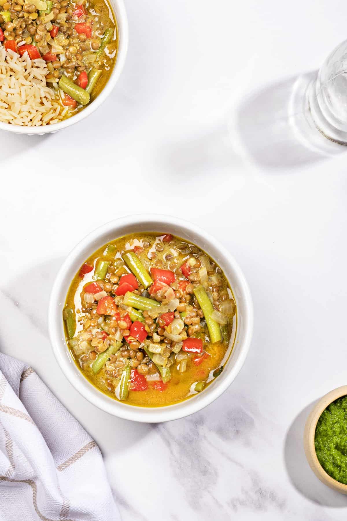 A birds eye view of a white bowl full of curried lentil soup with coconut on a white surface. | Hurry The Food Up