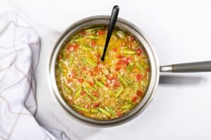 A saucepan full of curried lentil soup with coconut being cooked, with a big stirring spoon in it. | Hurry The Food Up