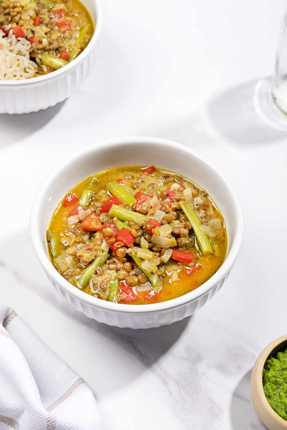 A bowl of curried lentil soup with coconut milk on a white surface, another bowl visible in the corner. | Hurry The Food Up