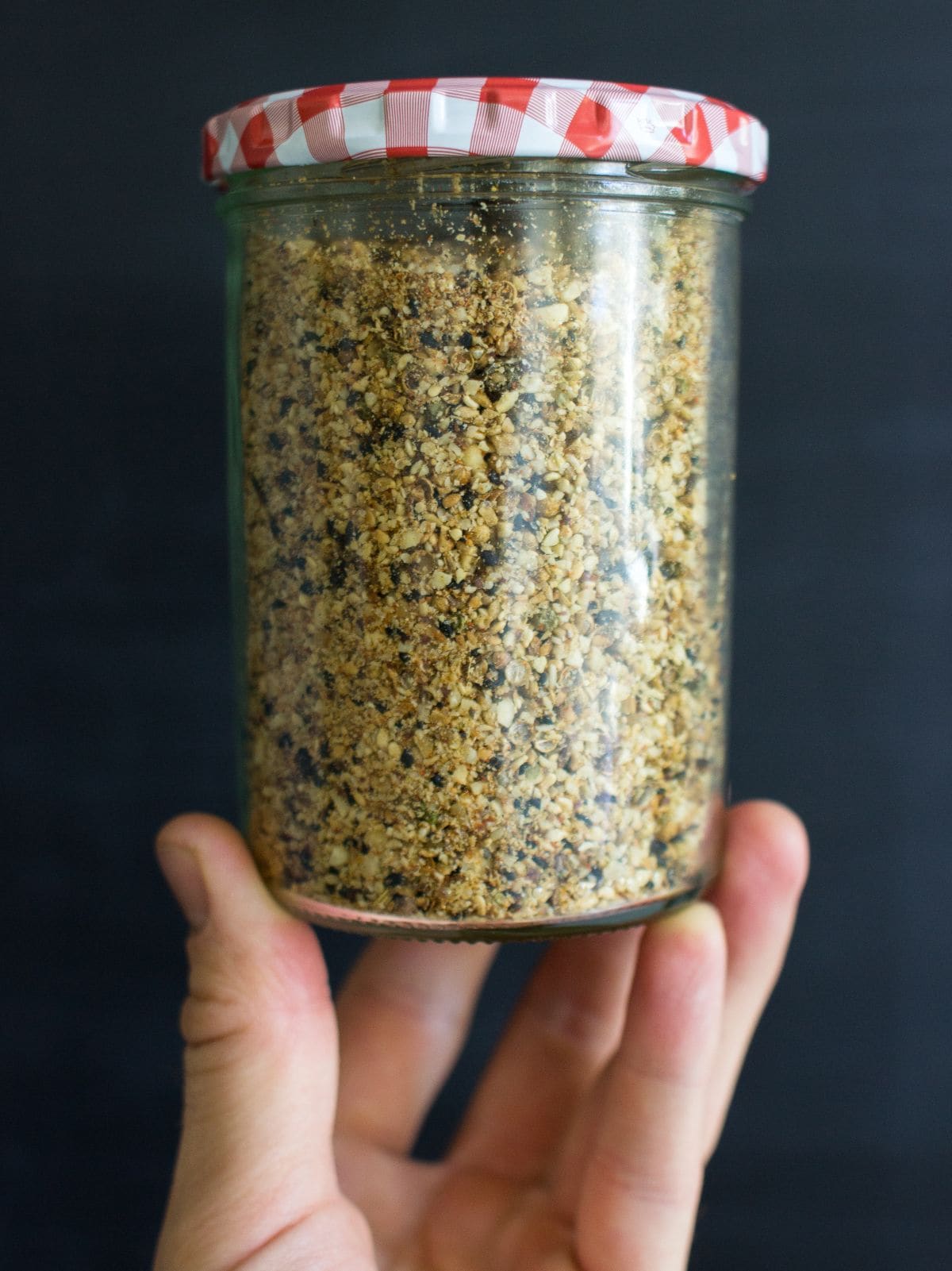 An old jam jar now filled with dukkah, held up by a hand | Hurry The Food Up