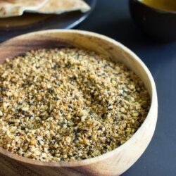 A wooden bowl filled with dukkah, with pittas in the background | Hurry The Food Up