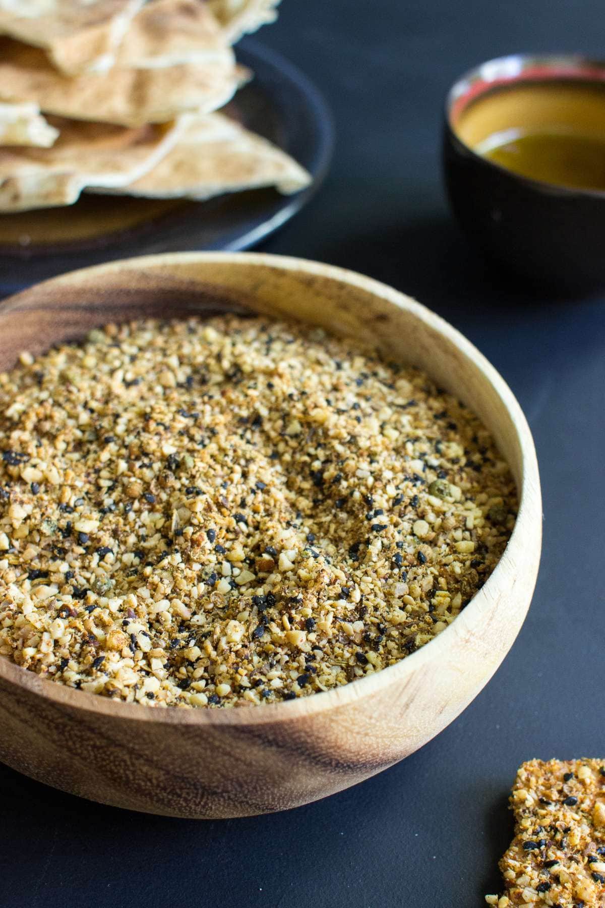 A wooden bowl filled with dukkah, with pittas in the background | Hurry The Food Up
