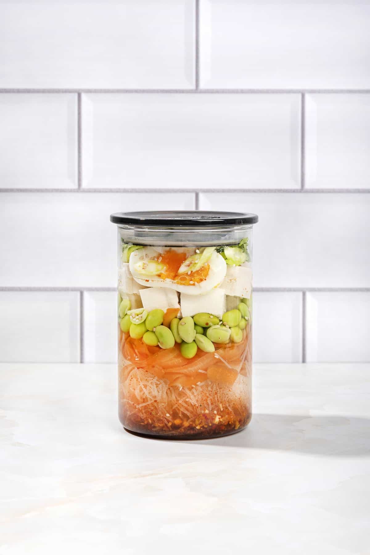 A sealed jar of all the constituent ingredients of an easy homemade ramen noodle soup, on a white surface | Hurry The Food Up