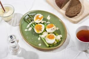 A landscape shot of a plate of boiled asparagus topped with jammy boiled eggs and drizzled with sauce | Hurry The Food Up