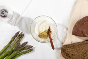 Sour cream, mustard and sugar ready to be mixed in a glass bowl. Asparagus stems and bread in the corners | Hurry The Food Up