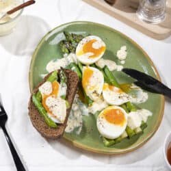 A plate of asparagus, jammy eggs, sour cream sauce and dark bread in the process of being eaten for breakfast| Hurry The Food Up
