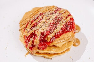 The process of pouring strawberry compote over stacked pancakes, drizzling some nut butter, and sprinkling with hemp seeds | Hurry The Food Up