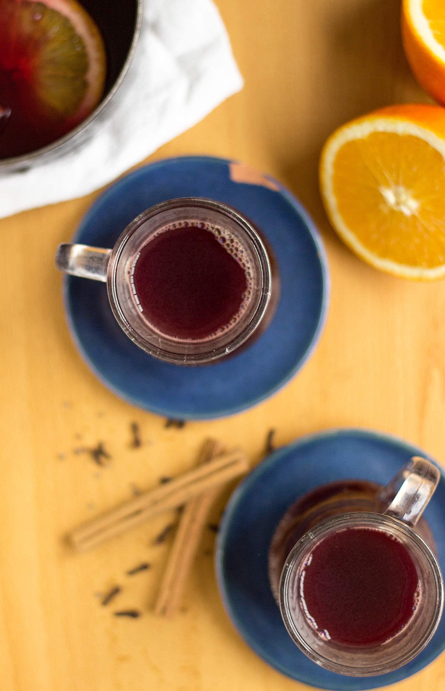 Spiced wine served in 2 glasses on blue plates with orange and cinnamon sticks on the table | Hurry The Food Up