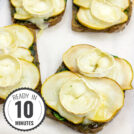 Slices of Honey Pesto Goat Cheese Toast, topped with creamy goat cheese, drizzled with golden honey, and garnished with fresh herbs, sit elegantly on a cutting board with a timestamp in the left corner.