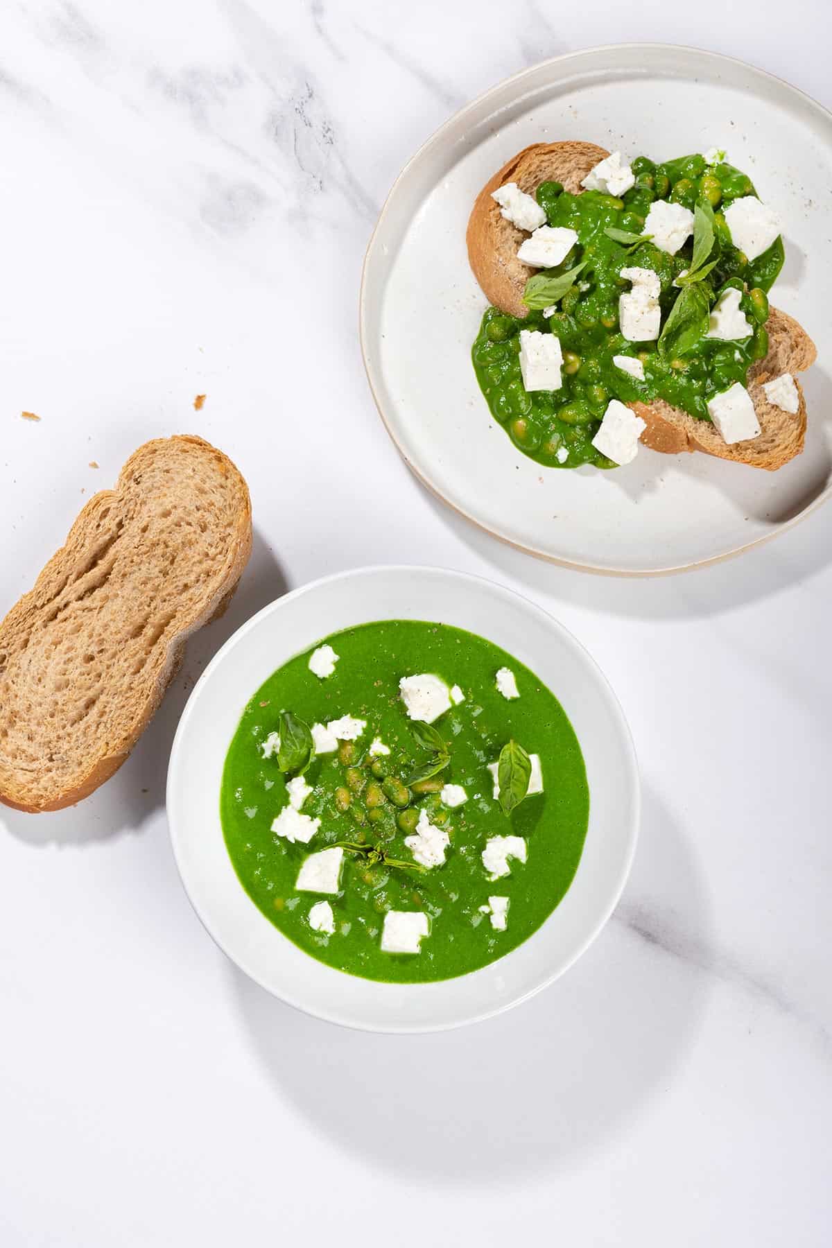 A birds eye view of toasted bread slice that is on the white plate is topped with beans, green sauce and crumbled cheese. There is a bowl with topping and a bread slice along it | Hurry The Food Up