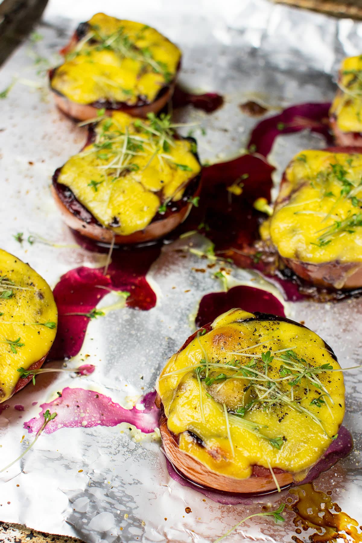 Grilled cherry tomatoes topped with melted yellow cheese and microgreens, served on a foil-lined baking tray with drizzles of savory blueberry jam.